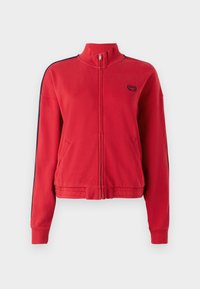 Giacca rossa con zip e colletto alto, dotata di strisce laterali blu navy e un piccolo logo sul petto. Realizzata in tessuto morbido e testurizzato.