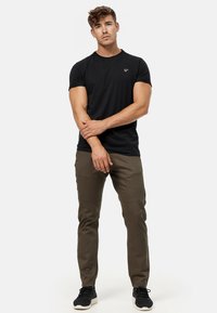 Camiseta de algodón negra combinada con pantalones verdes olivo, con costuras en las rodillas y zapatillas negras, sobre un fondo blanco plano.