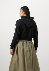 Sudadera corta negra con capucha, con rayas blancas en los laterales, combinada con una larga y fluida falda verde oliva con cintura elástica.