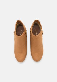 Botas de tornozelo castanhas feitas de camurça com uma textura suave. Apresentam um fecho lateral e um design de bico arredondado. Interior forrado para maior conforto.