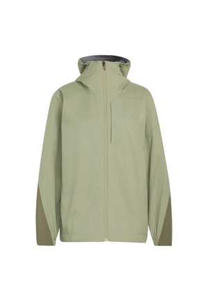 Kvinde iført lys grøn hættetrøje, sorte bukser og beige sneakers gående mod en ensfarvet lys baggrund.