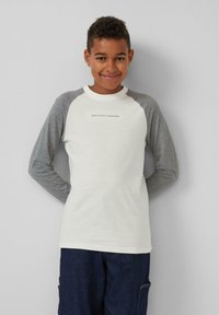 Weißes Langarmshirt mit grauen Raglanärmeln, das einen kleinen Textdruck in der Mitte aufweist. Weiches Material mit Rundhalsausschnitt.
