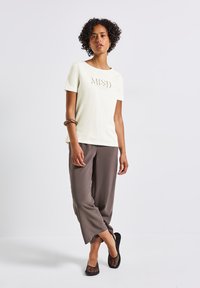 Light-colored t-shirt with "MIND" printed, paired with gray loose-fitting trousers and black mesh slip-on shoes. Smooth fabric textures.