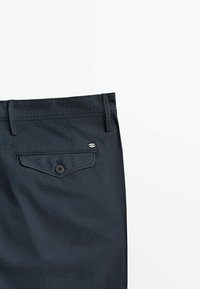 Laivaston siniset housut sujuvalla pinnalla, joissa on nappikiinnitys takataskussa ja huomaamattomat ompelu yksityiskohdat vyötäröllä ja taskuissa.