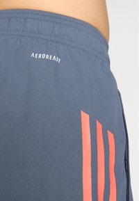 Et par blå atletiske shorts med et struktureret stof, elastisk talje og tre lodrette orange striber på siden.