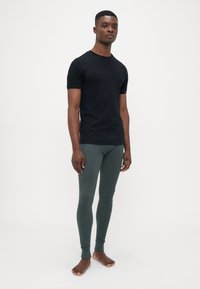 Musta lyhythihainen t-paita yhdistettynä tummanvihreisiin legginsseihin. Molemmilla vaatteilla on sileä pinta ja vartalonmyötäinen muotoilu. Jalat ovat paljaat.