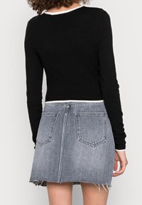 Svart långärmad topp med rundad halsringning, tillsammans med en grå denimkjol med fransad nederkant och två bakfickor.