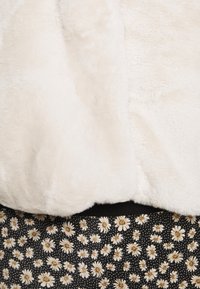 Tissu en fausse fourrure blanche douce au-dessus d'un tissu noir avec motif de marguerites blanches et beiges.