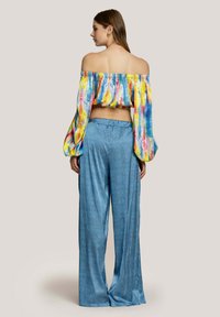 Top colorato senza spalle con un motivo tie-dye in blu, giallo e rosa abbinato a pantaloni a gamba larga blu chiaro, con un tessuto testurizzato.