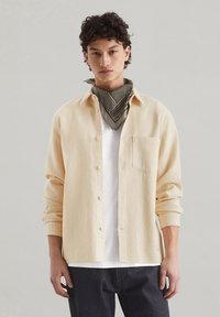 Cream-colored waffle-textured shirt with long sleeves, button-up front, and a single chest pocket, worn over a white t-shirt.