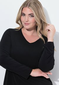 Schwarzes Langarmshirt mit V-Ausschnitt-Design, glatter Stoffstruktur und eng anliegenden Ärmeln, mit lockerer Passform in der Taille.