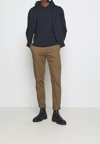 Marinblå polo skjorta lager på en mörk huvtröja, i kombination med beiga chinos och svarta ankelstövlar. Slät tyg med klassisk passform och uppvikta ärmar.