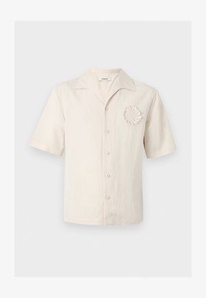 Lühikeste varrukatega kreemika linase särgiga, millel on sälkkaelus, ees nööbid ning vasakul rinnal dekoratiivne spiraalne heegeldatud detail.