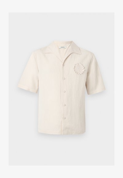 Πουκάμισο από λινό σε κρεμ απόχρωση με κοντά μανίκια, γιακά με εγκοπή, κουμπιά μπροστά και διακοσμητικό σπιράλ πλέγμα στο αριστερό μέρος του στήθους.