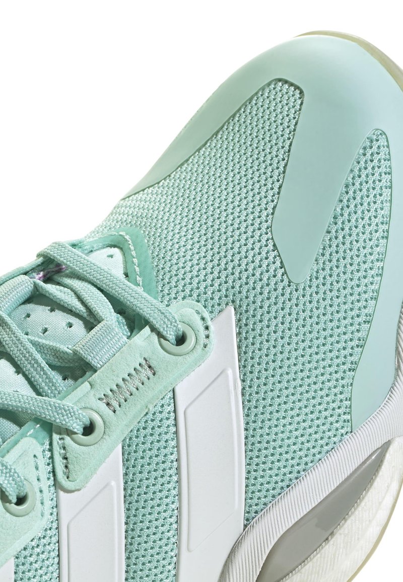 Hellgrüner Sportschuh mit einem Obermaterial aus Mesh, glatten weißen Akzenten, strukturierten Schnürsenkeln und einer Gummisohle mit leicht erhöhtem Absatz.