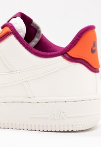 Sneaker bianca in pelle con suola texturizzata, caratterizzata da accenti viola e arancione, colletto imbottito e logo "AIR" in rilievo sul tallone.