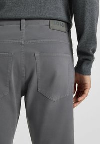 Szare spodnie z mieszanki bawełny, posiadające dwie tylne kieszenie oraz metkę z logo na pasku. Tekstura wydaje się gładka i miękka.