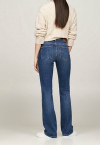 Jeans acampanados de color azul oscuro con cintura alta y detalles en el bolsillo trasero, combinados con un suéter de punto de cable ligero y zapatillas blancas.