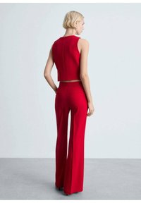 Červený dvoudílný outfit skládající se z krátkého bezramínkového topu a rozšířených kalhot s vysokým pasem, obojí vyrobené z hladkého, přiléhavého materiálu.