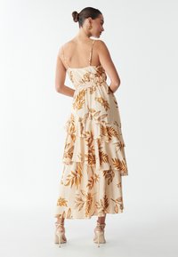 Abito beige chiaro con rouches sovrapposte e stampa floreale in oro e marrone. Spalline sottili regolabili e vita aderente.