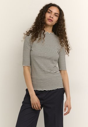 Gestreepte ribbeltrui in crème en zwart, met korte mouwen en een gegolfde halslijn. Gepaard met donker gestreepte pantalon.