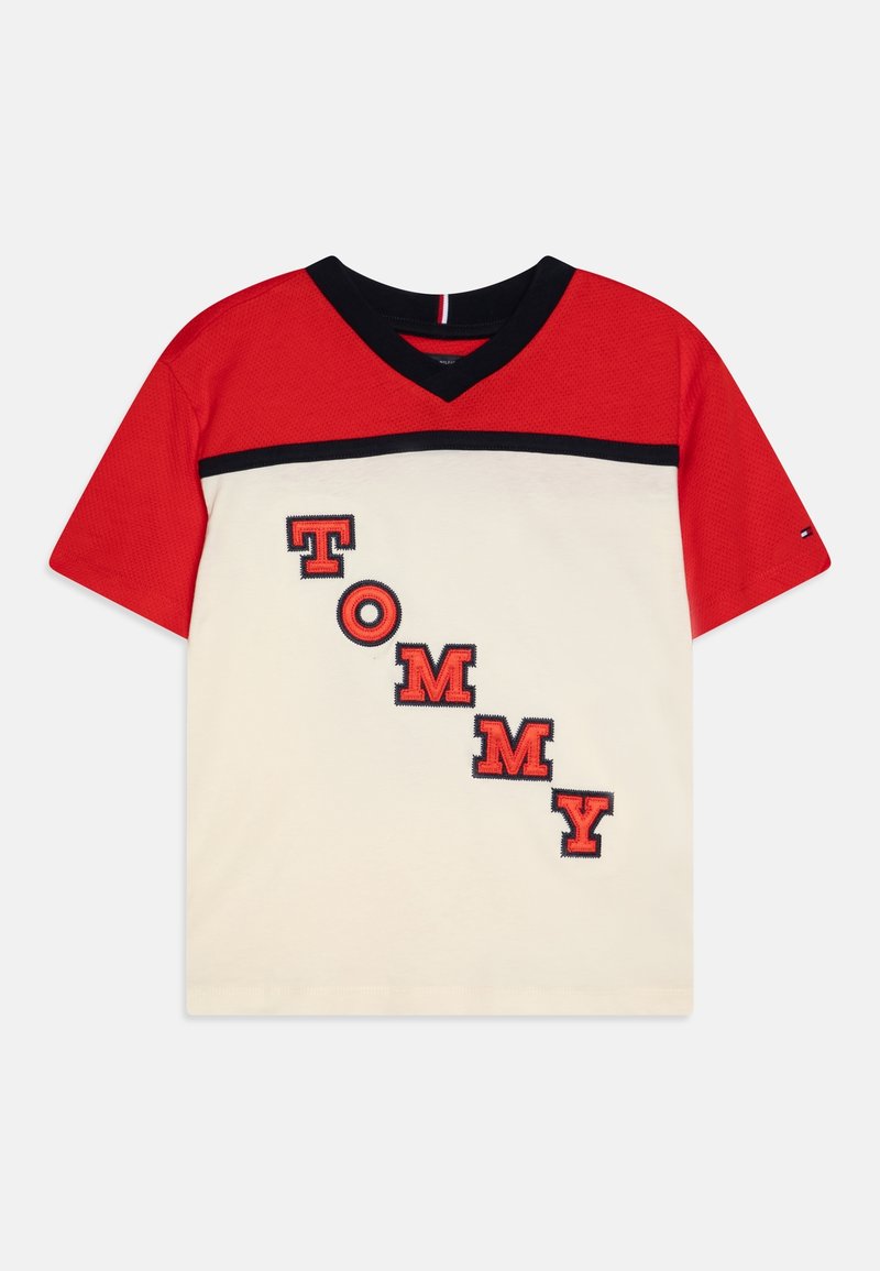 Maglietta a maniche corte rossa e bianca con scollo a V nero, striscia nera e la scritta "TOMMY" in grandi lettere rosse diagonali sul davanti.