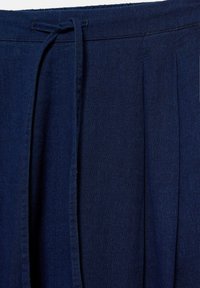 Pantalon en tissu bleu foncé avec une ceinture à la taille et une ceinture en tissu nouée au centre devant.