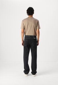 Dark gray jeans with a relaxed fit, paired with a light brown short-sleeve t-shirt. Features include back pockets and white sneakers.