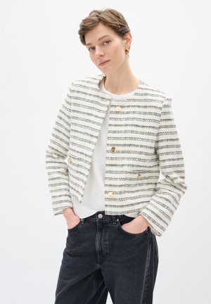 Weiß gestreifter Blazer mit blauen Linien, goldenen Knöpfen, tailliertem Schnitt und strukturiertem Stoff. Kombiniert mit einem weißen Oberteil und schwarzen Jeans.