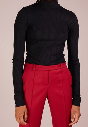 Person wearing a black ribbed long-sleeve turtleneck tucked into high-waist red tailored pants with belt loops.