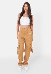 Kort-wit topje, gecombineerd met tan kleurige corduroy cargo pants met zijzakken, strikken en geborduurde branding. Witte sneakers maken de look compleet.