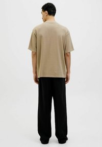 Beige bomulds t-shirt med kortærmer og en afslappet pasform, parret med løse sorte bukser. Glat tekstur, enkelt design, ingen synlige mønstre.