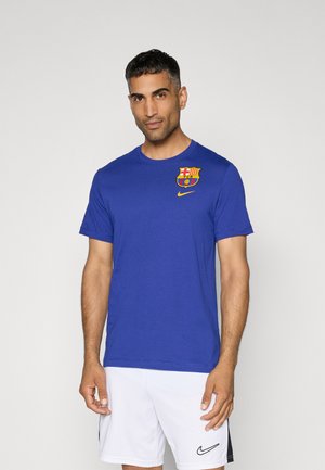 T-shirt in cotone blu con colletto rotondo, decorato con il logo giallo della Nike e un'emblema multicolore del FC Barcelona sul lato sinistro del petto.