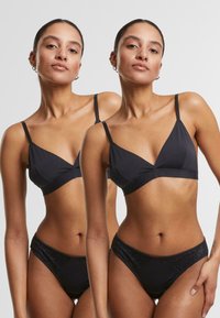 Svart, trekantet bralette med tynne stropper, som har en glatt tekstur. Kombinert med svarte høytalende bikiniunderdeler, også glatte.