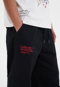 Czarne szorty z wyszywanym czerwonym logo "DON ED HARDY designs". Bawełnowy materiał o luźnym kroju i bocznymi kieszeniami. Prosty design, bez wzorów.
