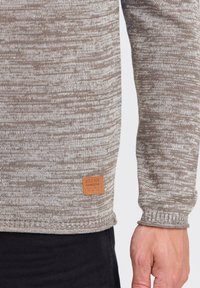 Strikket genser i blandede brune nyanser, med et strukturert mønster. Inkluderer et beige skinnmerke med "BLEND" sydd på kanten.