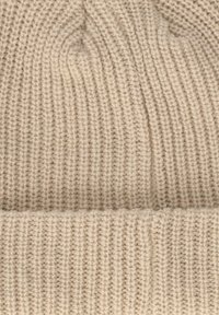 Beige gebreide beanie met een geribbelde textuur en een opgerolde rand. De stof lijkt zacht en flexibel, geschikt voor koud weer.