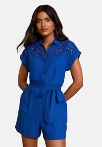 Modra lanena obleka s čipkastimi detajli na ramenih, kratkimi rokavi, sprednjim gumbom in zavezanjem v pasu. Gladka tekstura in sproščen kroj.