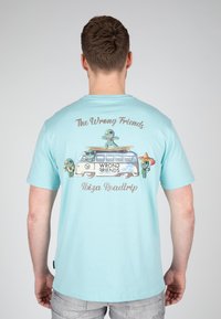Camiseta de color azul claro con un gráfico de cartoon que presenta una furgoneta y personajes, el texto dice "Los Amigos Equivocados Roadtrip a Ibiza". Mangas cortas, corte relajado.