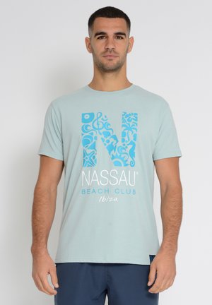 Lyseblå T-shirt med korte ærmer med et stort, mønstret "N" i turkis. Hvid tekst står der "NASSAU BEACH CLUB Ibiza" foran.