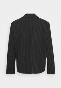 Blazer noir à fines rayures blanches, manches longues et col cranté, vu de dos sur fond blanc.