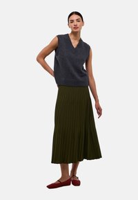 Haut en tricot sans manches gris avec un col en V, associé à une jupe plissée vert olive et des chaussures plates rouges. Design simple et épuré.