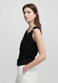 Černý top bez rukávů s drapérií po stranách, širokými ramínky a stříbrnými akcenty. Hladká tkanina s přiléhavým střihem.