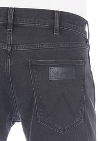 Czarne jeansy z denimu z tylną kieszenią z logo Wrangler i charakterystycznym wzorem przeszyć. Tkanina ma gładką fakturę.