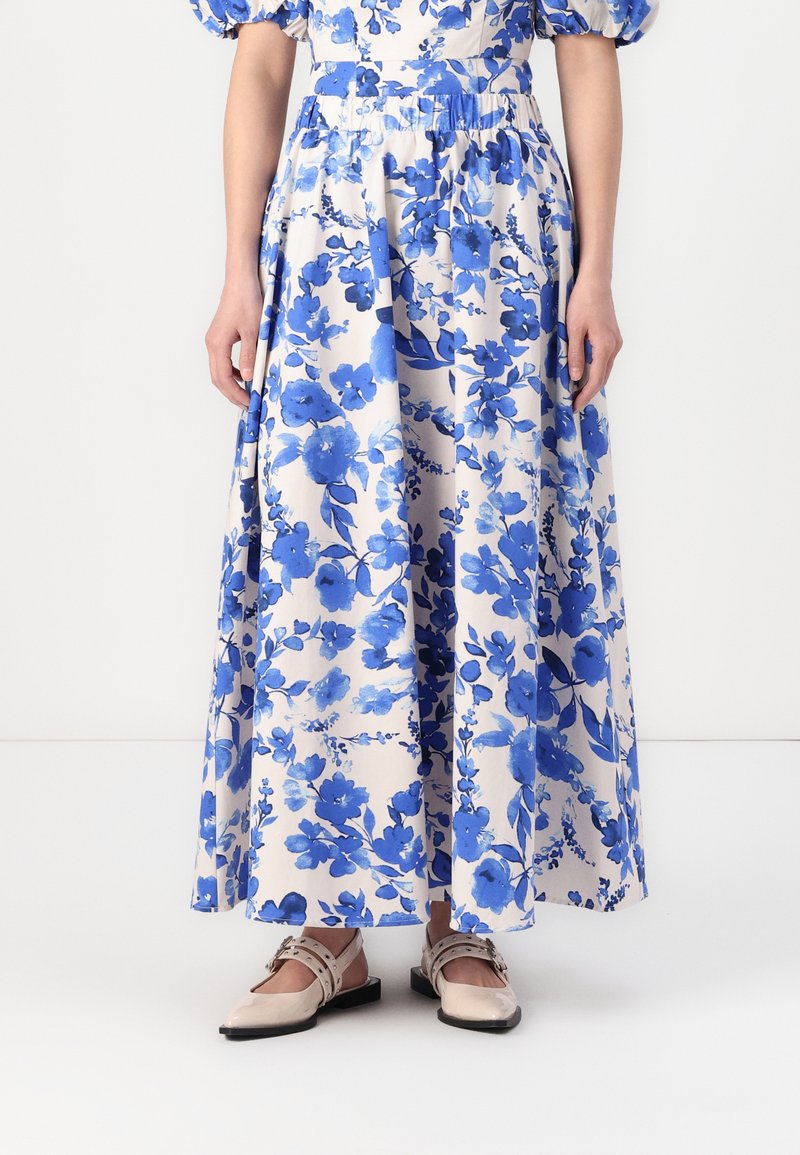 Robe maxi fleurie en crème avec des fleurs bleues, dotée de manches bouffantes et d'une taille froncée ; associée à des ballerines beiges avec un design de bride.