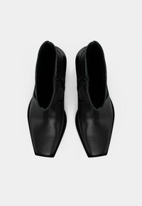 Melnas ādas potītes zābaki ar kvadrātu purngalu, gludu tekstūru un sānu rāvējslēdzējiem. Minimālistisks dizains bez redzamām rotājumām.