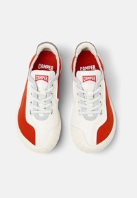 Vit sneaker med röda och grå accenter, med ett texturerat tygöverdrag, sydda detaljer och en gummisula med ett mönstrat mönster.