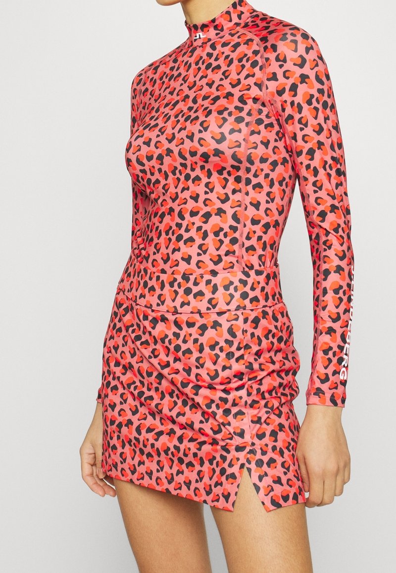 Long-sleeve, high-neck dress in a pink fabric with a black and red leopard print. Features ruching and side slits for movement.