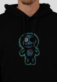 Czarna bluza z kapturem z wielokolorowym haftowanym wzorem lalki z niebieskim ciałem, czarnymi detalami i czerwonym sercem na piersi.