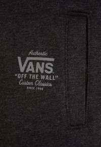 Ciemnoszara bluza z miękką teksturą, z białym nadrukiem logo, które brzmi "VANS 'OFF THE WALL' Custom Classics." Zawiera detal kieszeni.